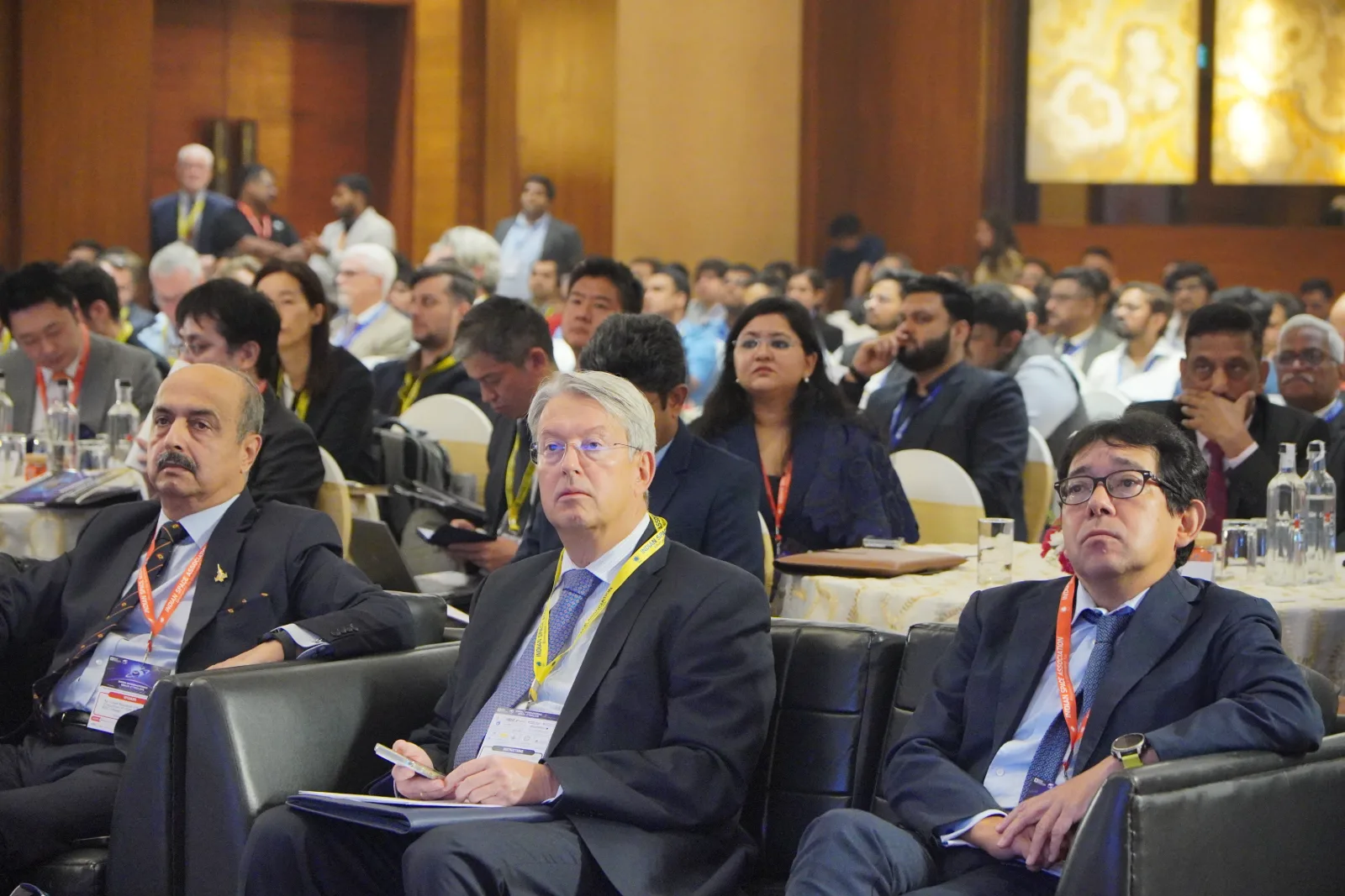 Delegates seated in the conference hall at IISC 2025 follow a session, lanyards around their necks.